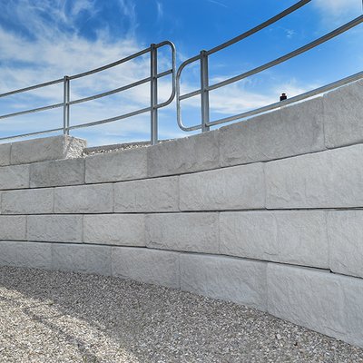 Solide Betonmauer mit geschwungener Absturzsicherung schützt den Weg entlang der Böschung