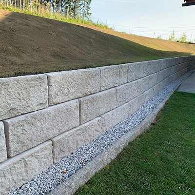 Betonblöcke zur Böschungssicherung mit sauber ausgeführtem Schotterstreifen entlang der Mauer