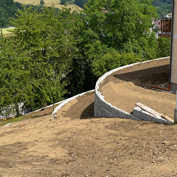 Gebogene Betonmauer sichert Gelände am Wohnhaus – Böschung in mehrere Flächen untergliedert